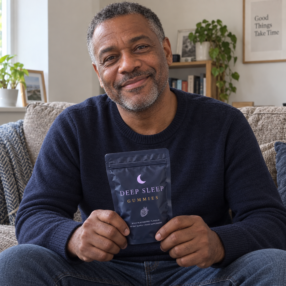 A smiling man relaxing on his sofa with a pouch of Deep Sleep Gummies